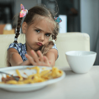 Une fille qui refuse de manger pousse une assiette de nourriture hors de la table, montrant qu'elle est une mangeuse difficile.