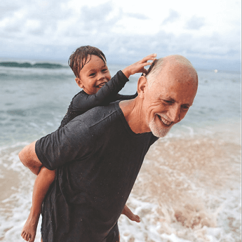 Older man carrying boy on his back with a beach and sea backdrop