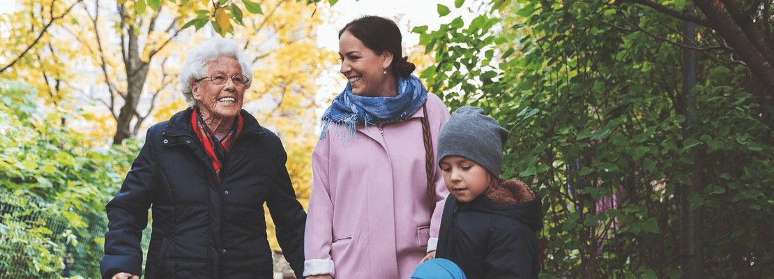 Old age, middle age and child together smiling on a walk in the forest with their coats on