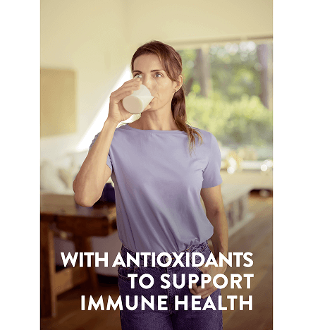 A woman drinks a white glass of pediasure vanilla in her living room with the words with antioxidants to support your immune system