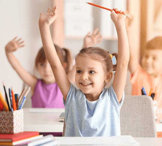 A number of children with both their arms in the air celebrating in a classroom