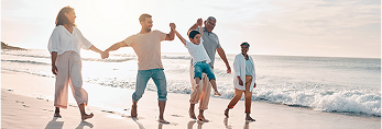 Een gezin met meerdere generaties loopt hand in hand langs het strand en zwaait met de jongen