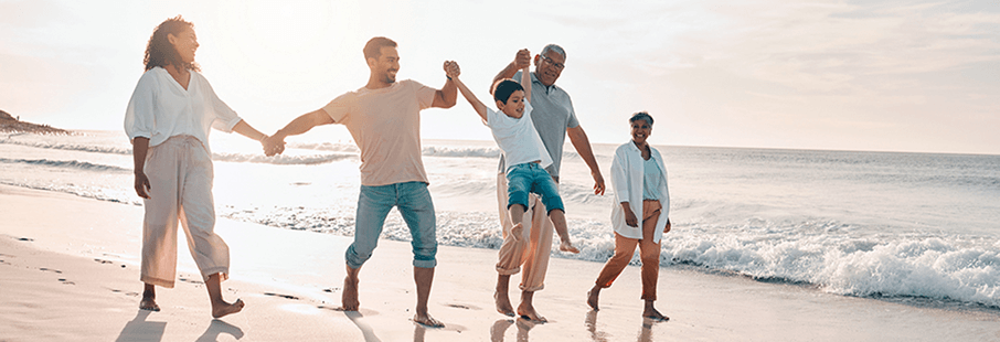 3 generaties familie wandelen langs het strand terwijl ze hun kind/kleinkind schommelen