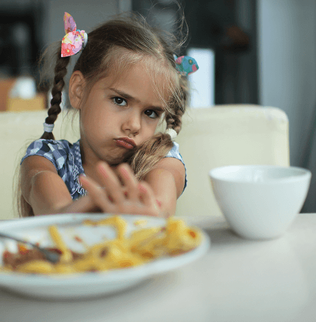 Een meisje dat weigert te eten, schuift een bord met eten terug over de tafel, wat laat zien dat ze een kieskeurige eter is
