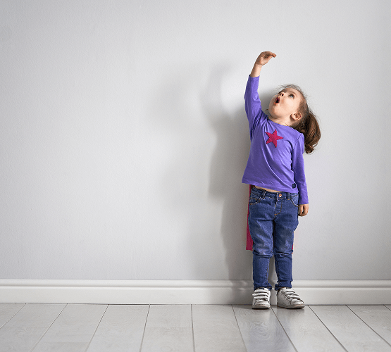 A young girl holds her hand high above her head showing surprise at her growth in height