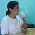 A woman wearing white shirt drinking a glass of Glucerna milk