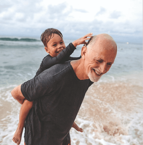 Un homme âgé portant un garçon sur son dos avec une plage et la mer en arrière-plan
