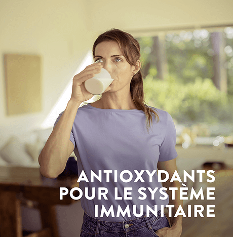 Une femme buvant un verre d'Assure avec un texte sur l'image soulignant les antioxydants pour le soutien de l'immunité