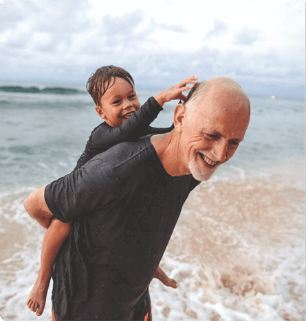 Older man carrying boy on his back with a beach and sea backdrop