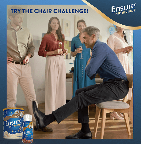A man crossing his arms and one leg out as he tries to do the chair challenge