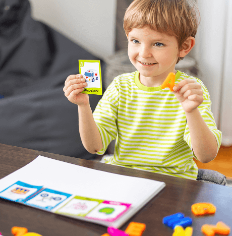 Boy demonstrating learning as he holds up a card with the letter A and a card with the picture of an ambulance