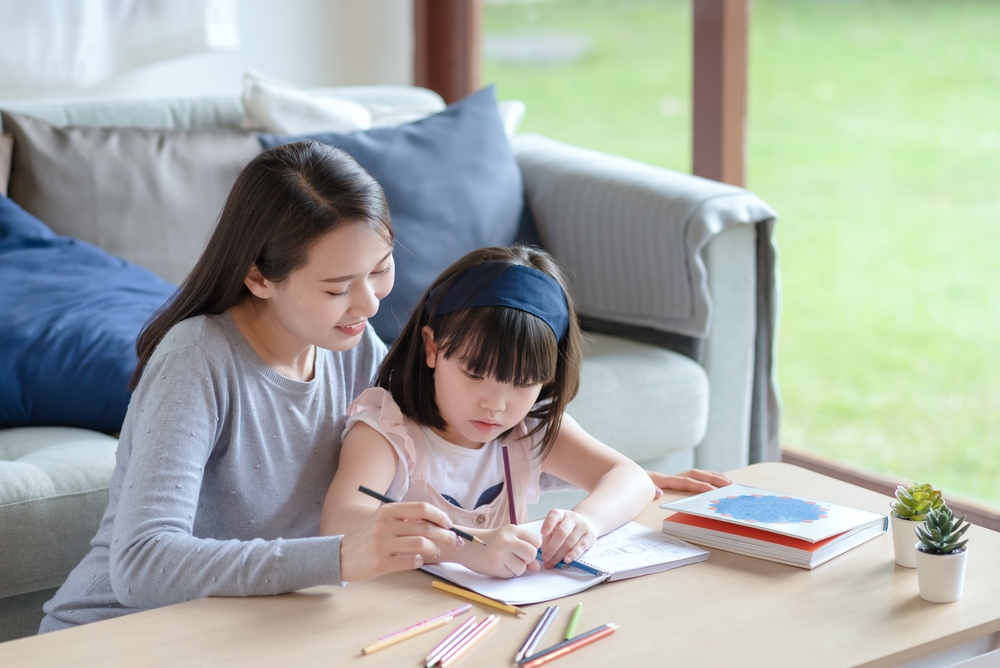 Asian mother teaching her cute kid daughter to studying in living room at home