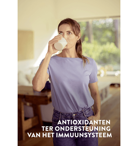 Een vrouw drinkt een wit glas Pediasure Vanilla in haar woonkamer met de woorden 'met antioxidanten ter ondersteuning van uw immuunsysteem'