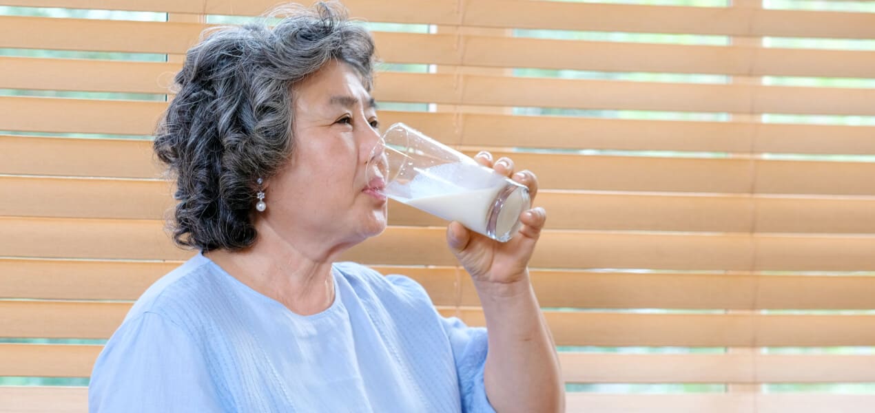 An elder woman wearing blue top while drinking a glass of Glucerna milk