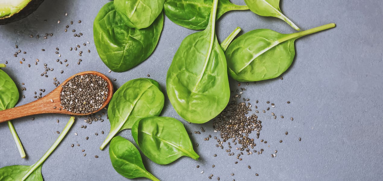 Scattered spinach leaves with a wooden spoon full of chia seeds at the side